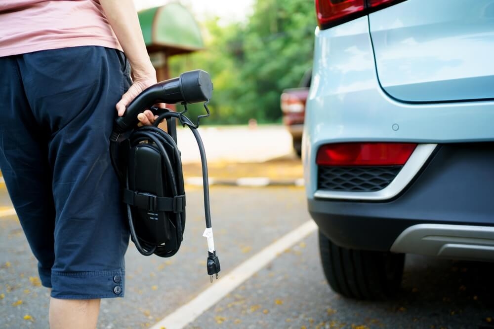 pessoa segurando um carregador elétrico e caminhando em direção ao seu carro